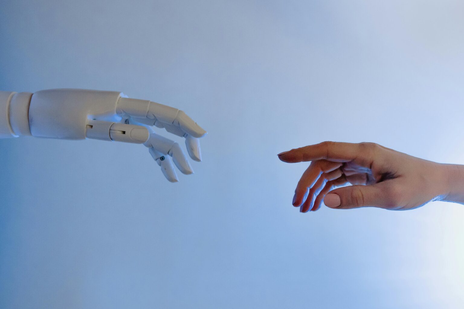 A robotic hand and a human hand reaching toward each other against a blue background, symbolizing AI and human collaboration