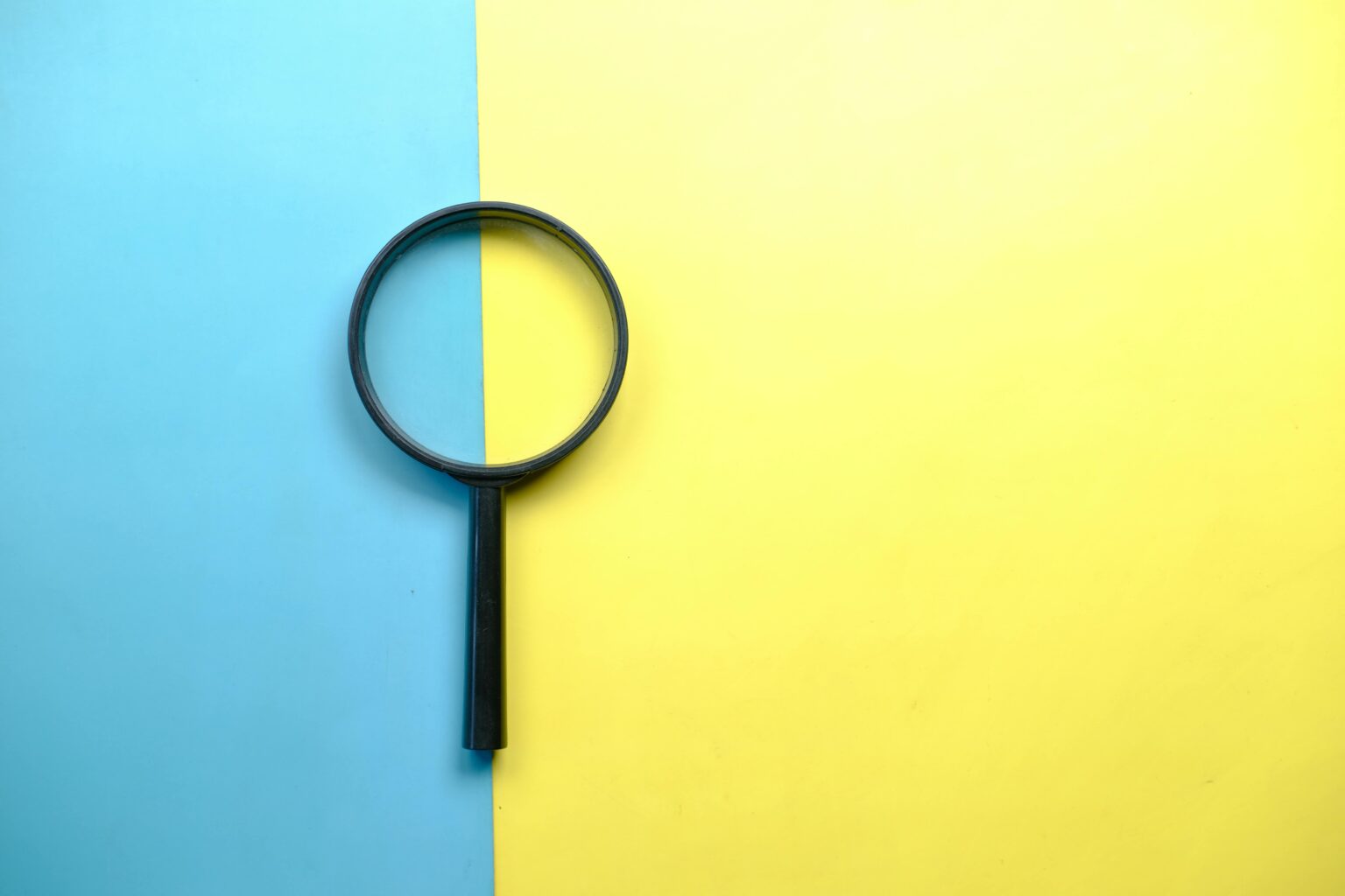 A magnifying glass resting on a two-tone blue and yellow background, symbolizing a close comparison between two website platforms